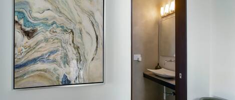 Un baño con una obra de arte de mármol en la pared, un lavabo y un espejo con luces.