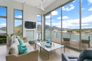 Relax in a serene space with expansive views of water and mountains, featuring a flat-screen TV and comfortable seating.