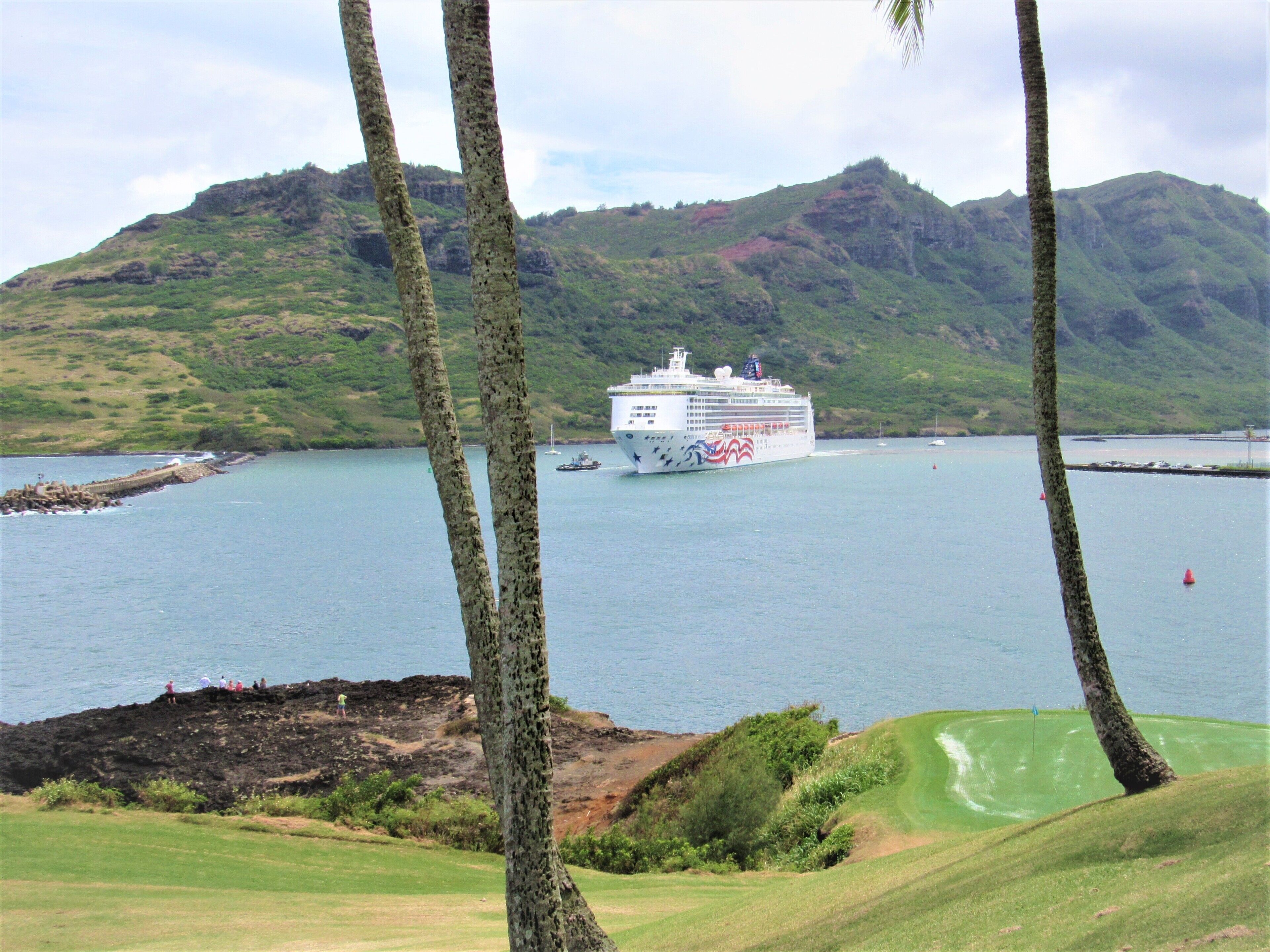 Un crucero amarrado en un puerto con montañas al fondo y un campo de golf cercano.
