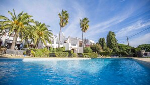 A swimming pool with clear blue water, surrounded by palm trees and a white building with balconies. - BayMar - Alojamientos MarCalm (Mont-roig Bahia)