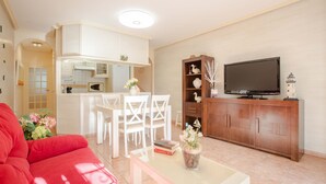 A living room with a red sofa, a glass coffee table, a TV on a wooden cabinet, and a white dining area with chairs. - BayMar - Alojamientos MarCalm (Mont-roig Bahia)