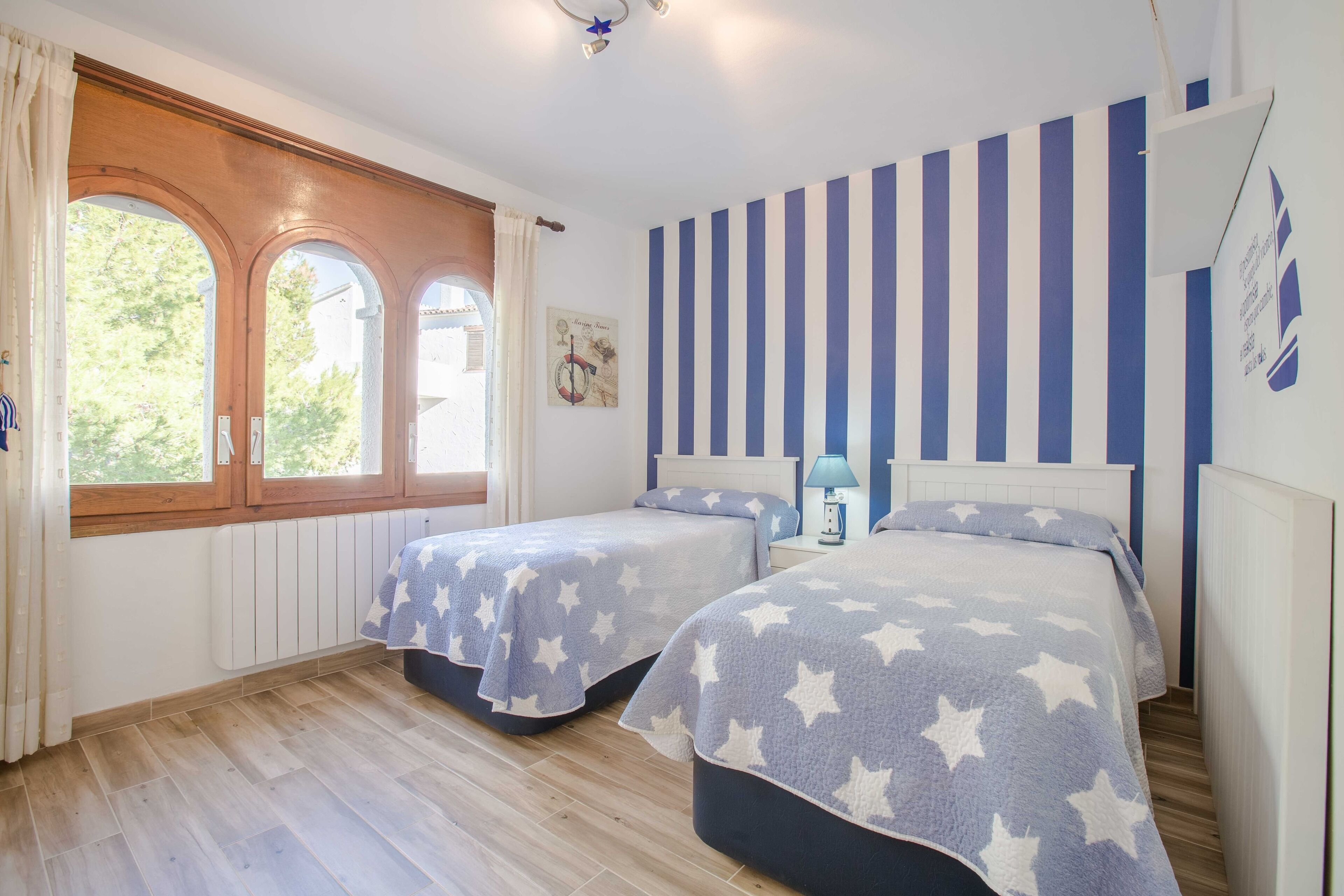 A bedroom with two beds, a window with curtains, a radiator, and a striped wall.