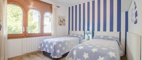 A bedroom with two beds, a window with curtains, a radiator, and a striped wall.