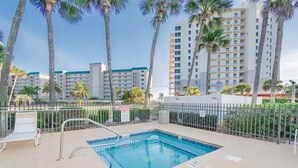 A swimming pool with a metal fence, surrounded by palm trees and a building with multiple floors in the background. - Beautiful views of beach, sunset, sunrise and the Blue Herons at the pond... (Pensacola)