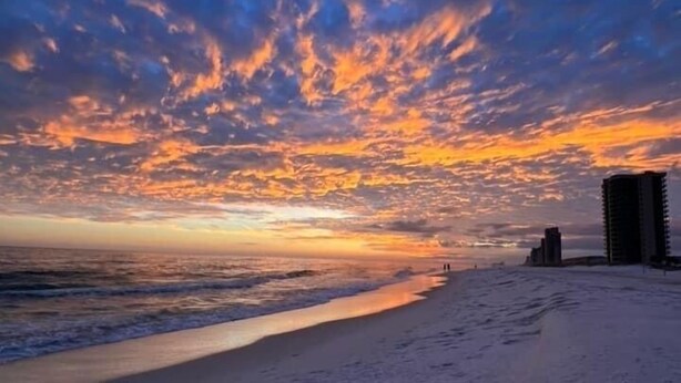 A beach with a sunset, ocean waves, and a few buildings in the distance. - Beautiful views of beach, sunset, sunrise and the Blue Herons at the pond... (Pensacola)