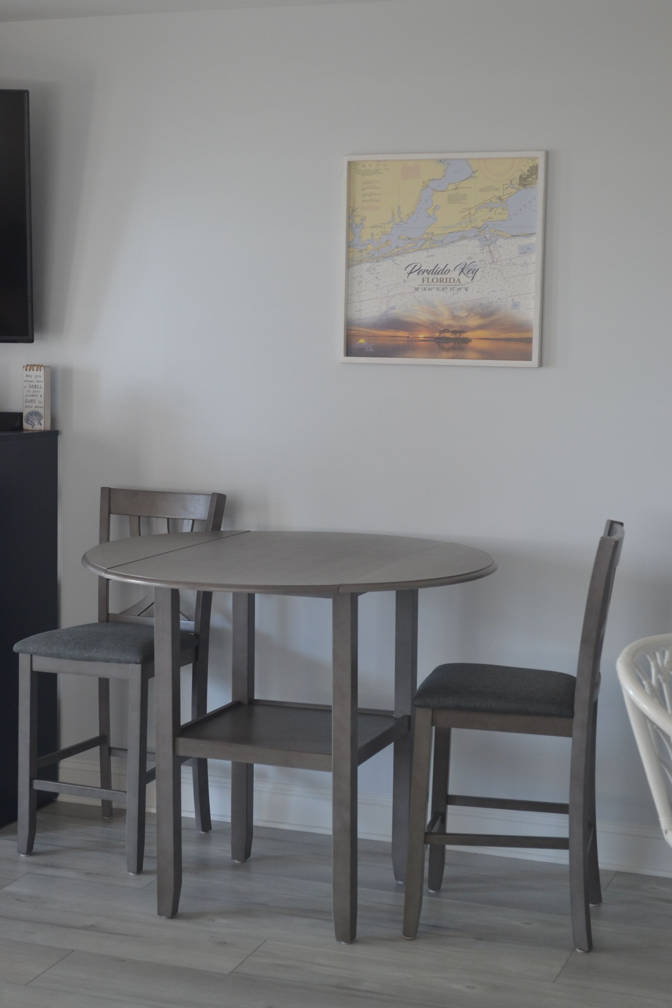 Un coin repas avec une table ronde et quatre chaises. Une carte de la Floride, encadrée, est accrochée au mur.