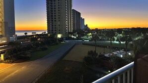 A high-rise building with multiple balconies, a road in the foreground, and a sunset in the background. - Beautiful views of beach, sunset, sunrise and the Blue Herons at the pond... (Pensacola)