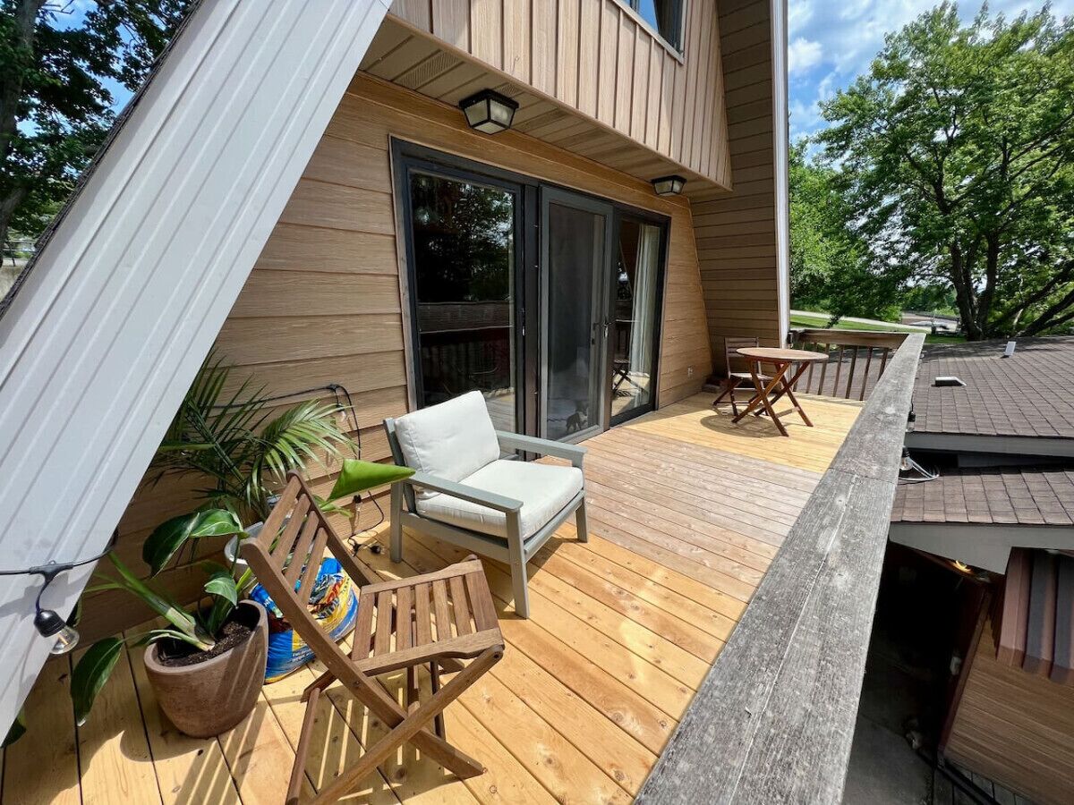 A wooden deck with a chair and a table, a potted plant, and a large window.