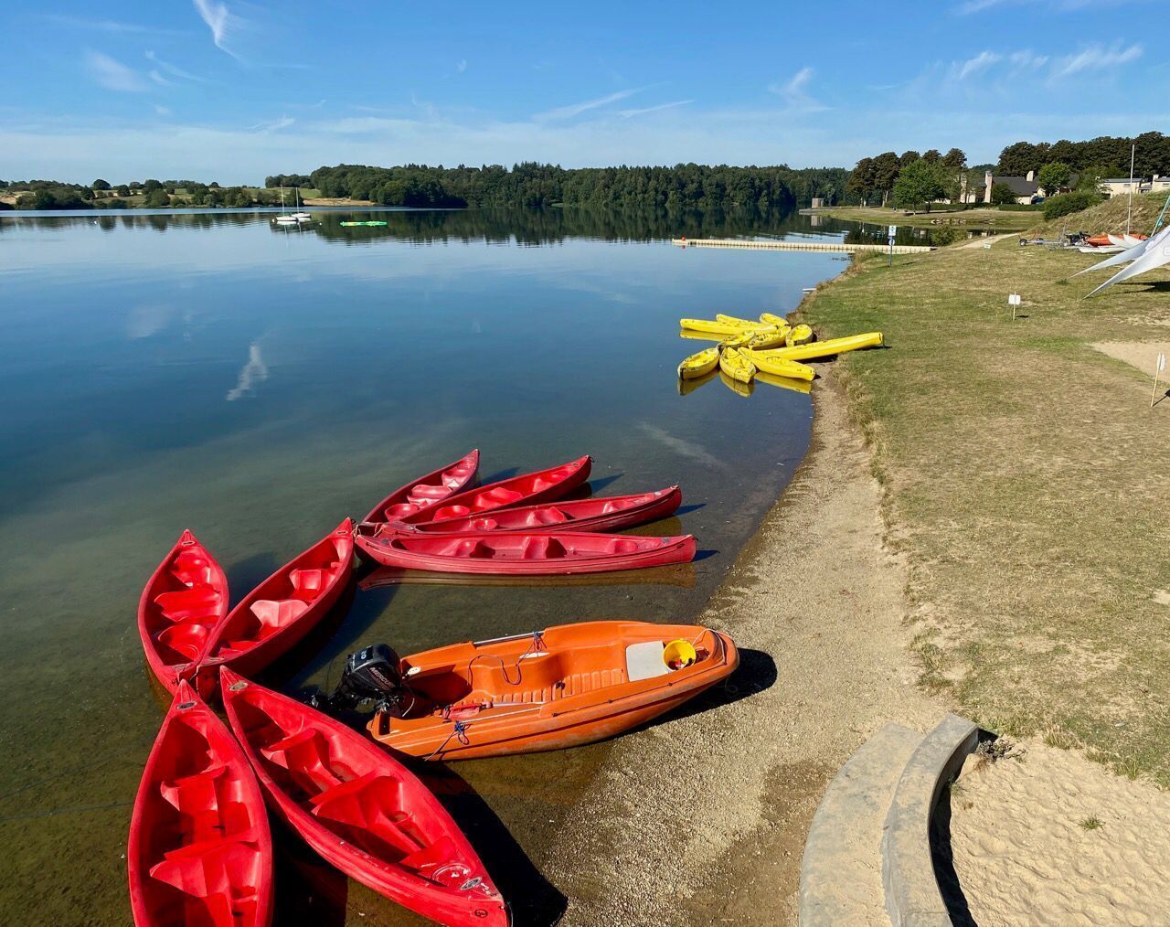 A calm lake with several kayaks and a small boat docked at the shore.
