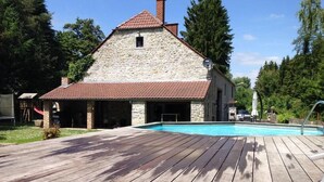 Un bâtiment en pierre, doté d’un toit recouvert de tuiles rouges et d’une terrasse en bois qui mène à une piscine.