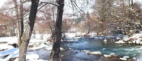 A river flowing through a snowy landscape with bare trees.