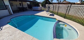 Une piscine avec un jacuzzi, entourée d’un patio agrémenté de chaises et d’un espace salon couvert.