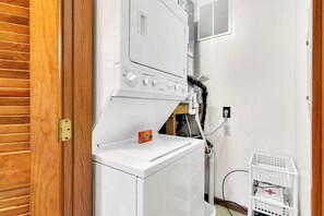 A laundry room with a white washer and dryer, a wooden door, and a white laundry basket.