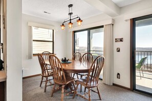 A dining area with a round table and six chairs, a ceiling light fixture, and a large sliding glass door leading to an outdoor balcony.