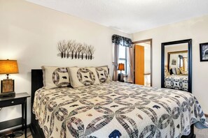 A bedroom with a bed, a nightstand, a wall-mounted lamp, a mirror, and a door leading to another room.
