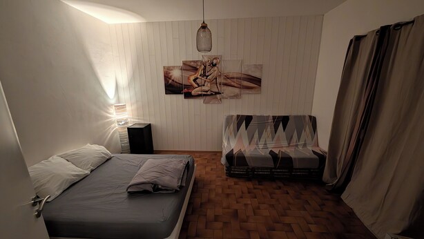 Une chambre à coucher comprenant un lit, un canapé, un haut-parleur fixé au mur, un luminaire suspendu et un tableau.