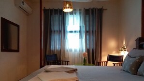 Ein Hotelzimmer mit einem Bett, einem Sessel, einem Tisch, einer Lampe und einem fenster mit Vorhängen.