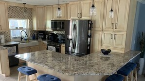 Uma cozinha com ilha de granito, eletrodomésticos de aço inoxidável e banquetas azuis.