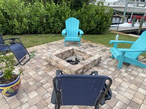 Un patio con una chimenea, dos sillas Adirondack azules y una planta en maceta.