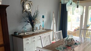 Uma área de refeições com uma mesa de madeira, cadeiras brancas, um armário branco e objetos decorativos.