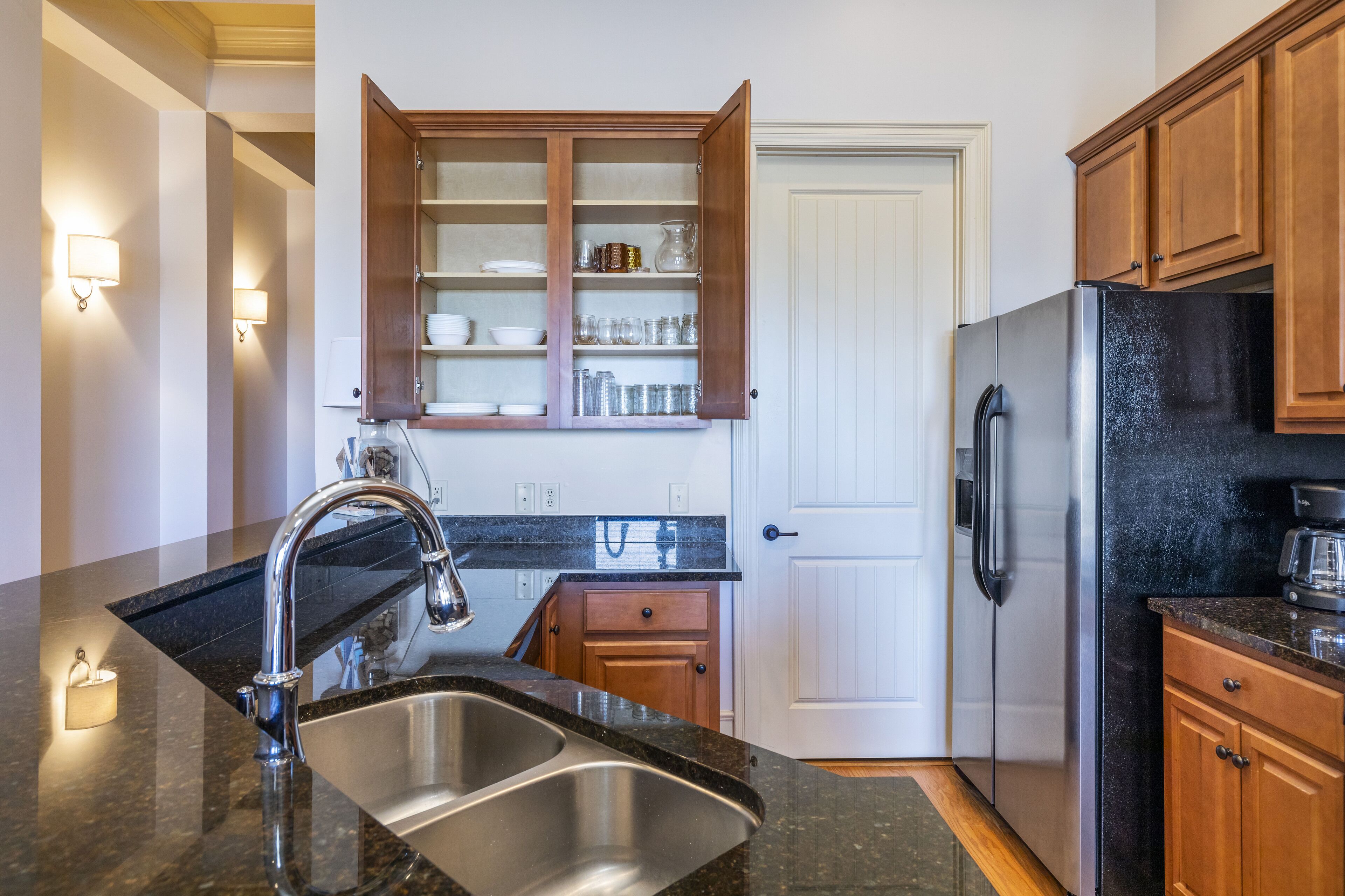 A modern kitchen with a stainless steel sink, wooden cabinets, and a black refrigerator.