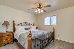 Ein Schlafzimmer mit Bett, Nachttisch, Lampe, Deckenventilator und Fenster.