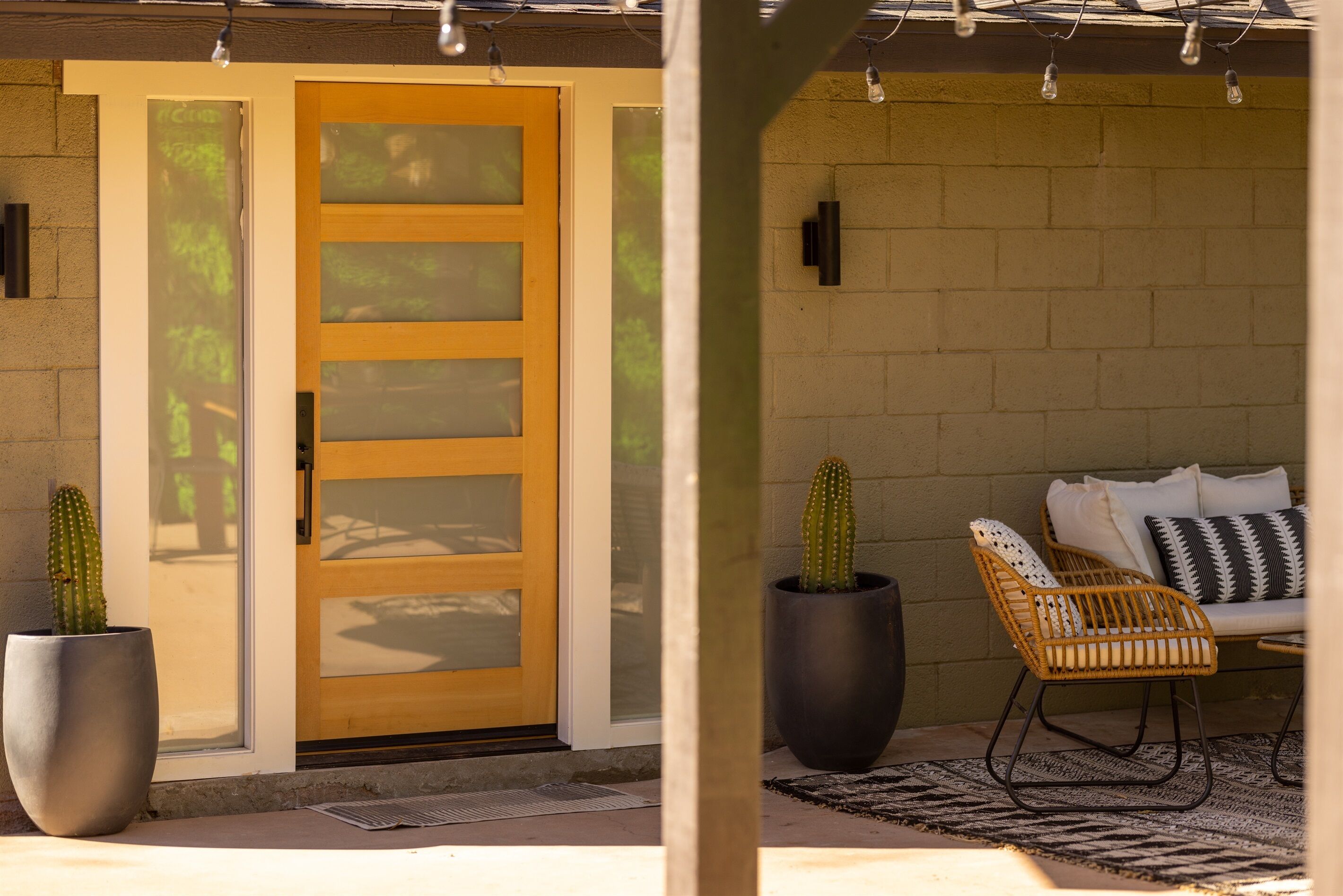 A patio area with a wooden door, two potted cacti, a wicker chair, and a patterned rug.