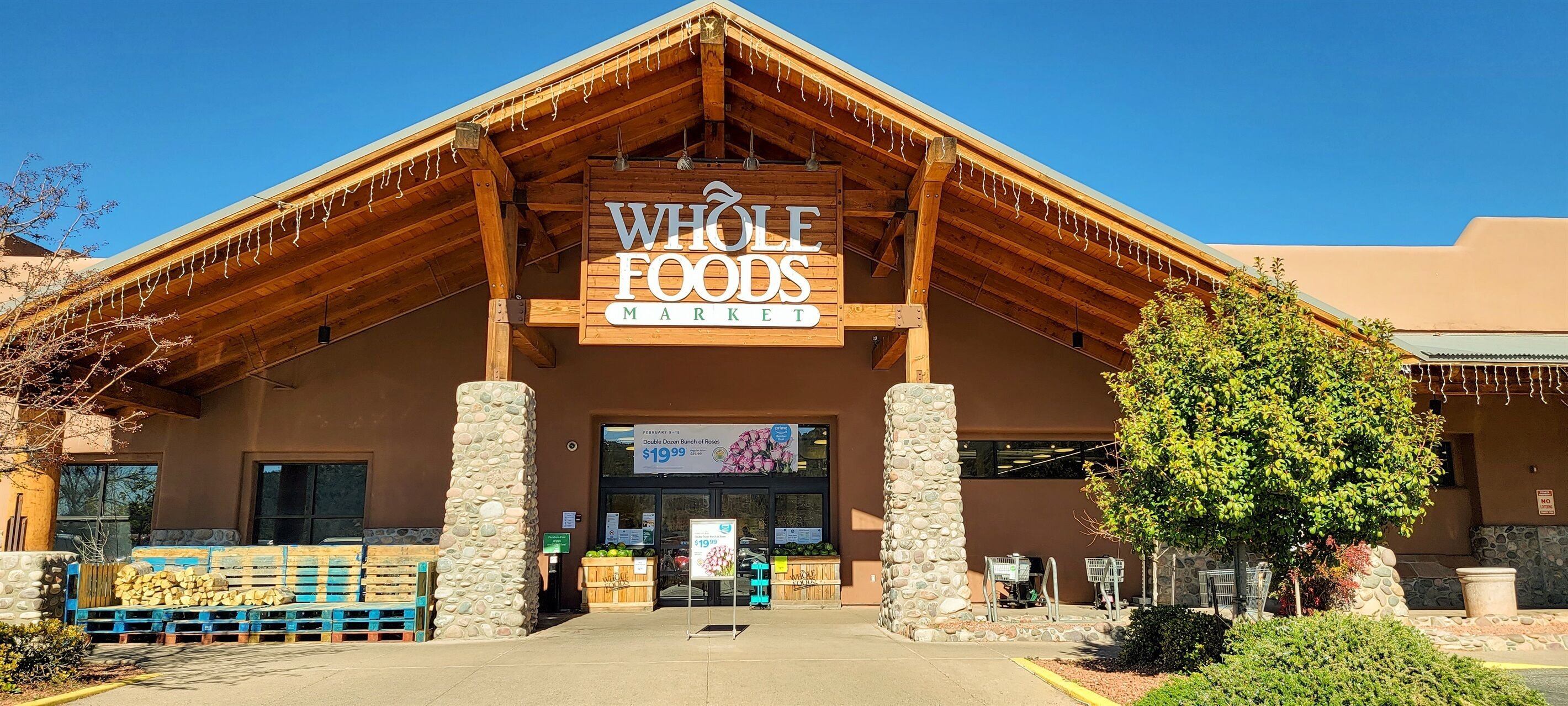 Un magasin Whole Foods Market avec une façade en bois, des piliers en pierre et un ciel d’un bleu éclatant.