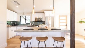 A modern kitchen with white cabinets, stainless steel appliances, and a central island with stools. - Designer Bungalow in Heart of Sedona, Enclosed Yard/Patio, Luxe Kitchen (Sedona)