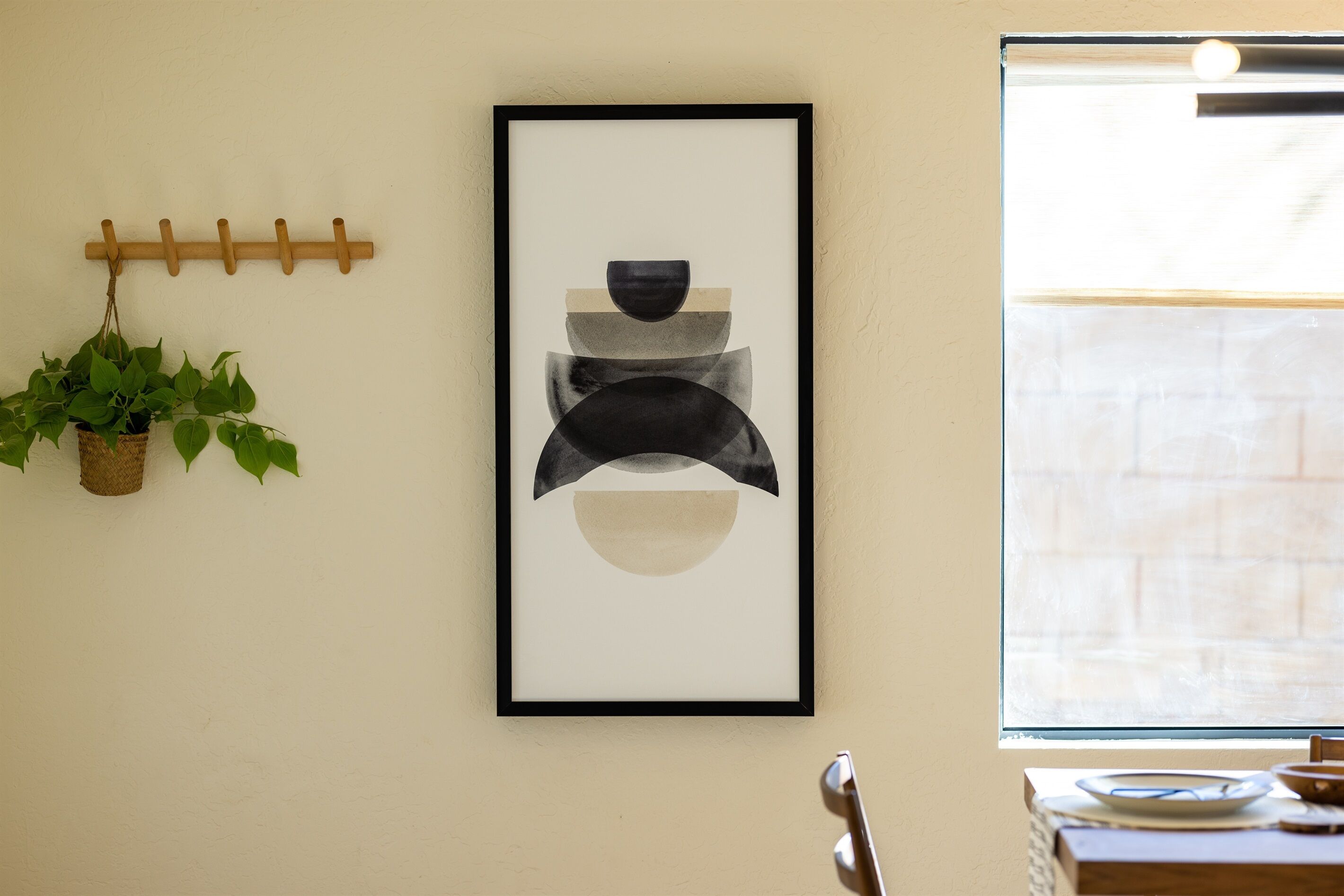 A framed abstract artwork on a wall, a wooden coat rack, and a potted plant.