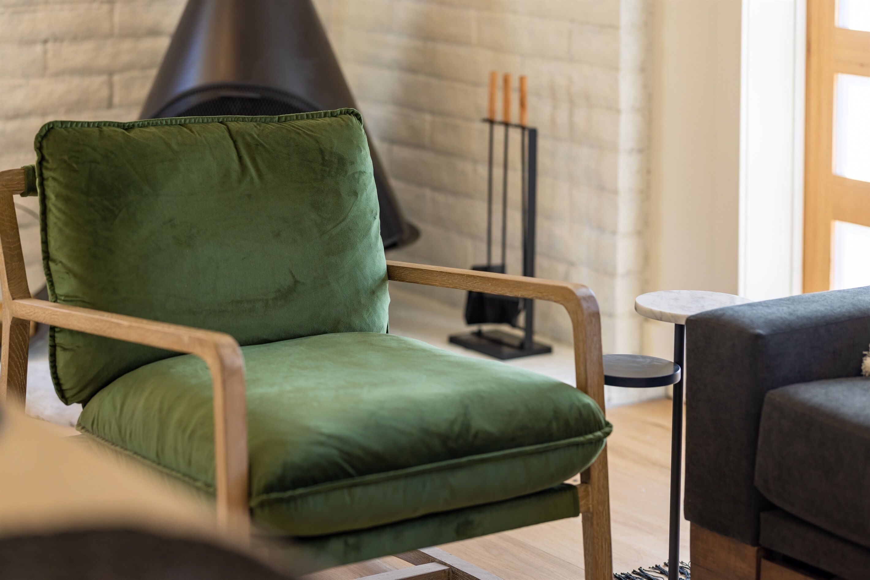 A green upholstered chair with a wooden frame in a room with a brick wall and a black fireplace.