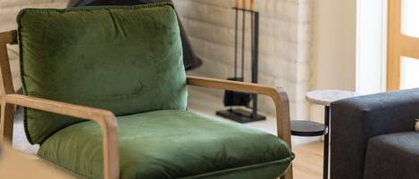 A green upholstered chair with a wooden frame in a room with a brick wall and a black fireplace.