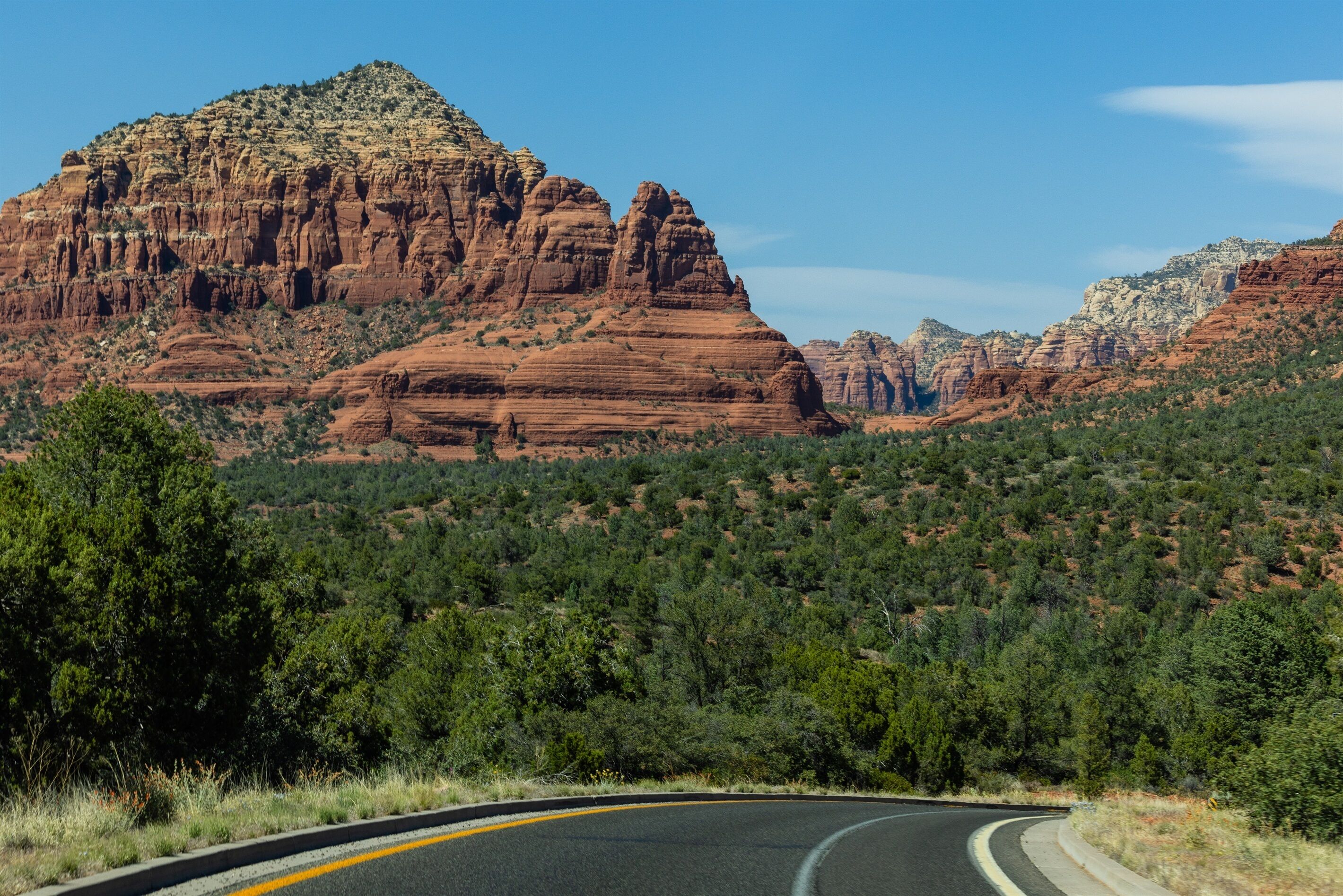 A winding road with red rock formations and green vegetation.