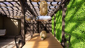 A covered outdoor area with a wooden floor, black metal chairs, and a green wall. - Designer Bungalow in Heart of Sedona, Enclosed Yard/Patio, Luxe Kitchen (Sedona)