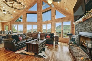 Un salón espacioso con un gran techo de madera, una chimenea y vistas a las montañas.