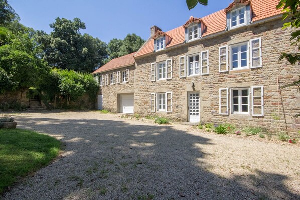 A stone building with a gravel driveway, a garage, and a small garden area.
