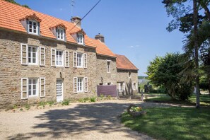 A stone building with a red-tiled roof, multiple windows, and a gravel driveway.