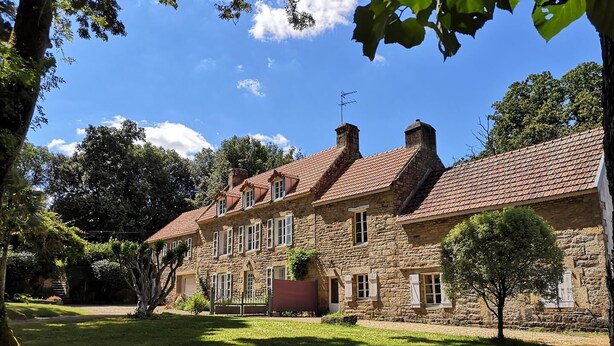 Um edifício de pedra com telhado em telhas, várias janelas e um gramado bem cuidado.