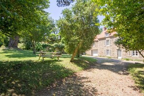 A stone building with a paved driveway and a picnic table in a lush garden.
