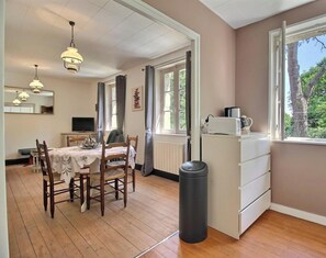 A room with a wooden floor, a dining table with chairs, a kitchen area with a microwave, and a trash bin. - Le Cosy - LOCOAL-MENDON (LOCOAL-MENDON)