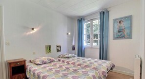 Una camera da letto con un letto, un comodino, una finestra con tende e un quadro appeso al muro.