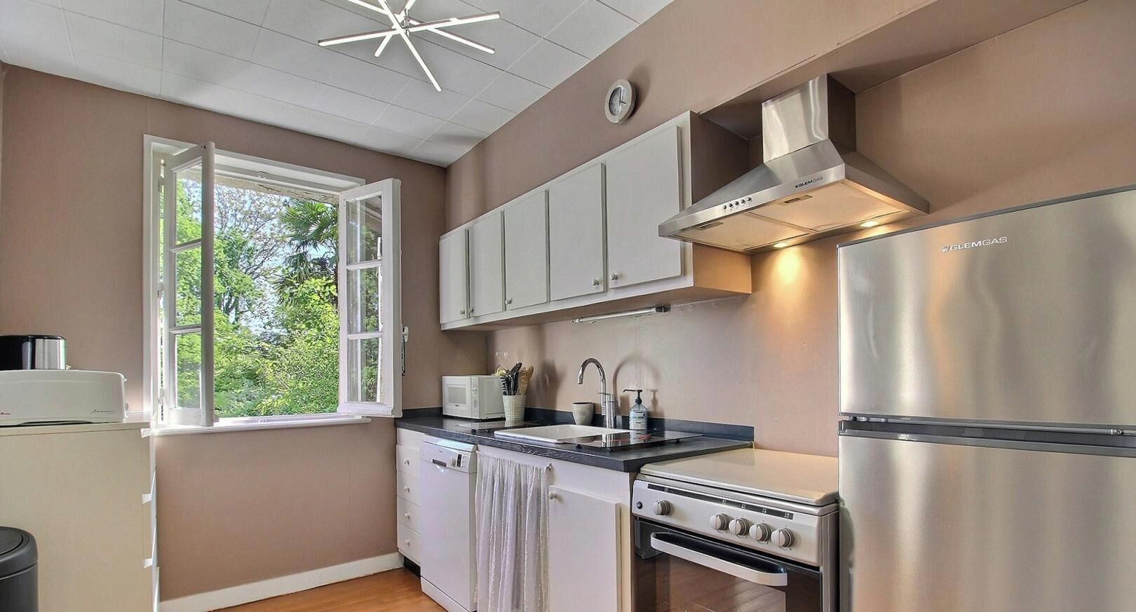 A modern kitchen with white cabinets, a stainless steel refrigerator, a built-in oven, and a window with a view of greenery.