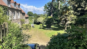 Un edificio in pietra con tetto in tegole rosse, circondato da vegetazione lussureggiante e alberi.