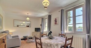 Una stanza con un tavolo da pranzo, sedie, una televisione e una finestra con tende.