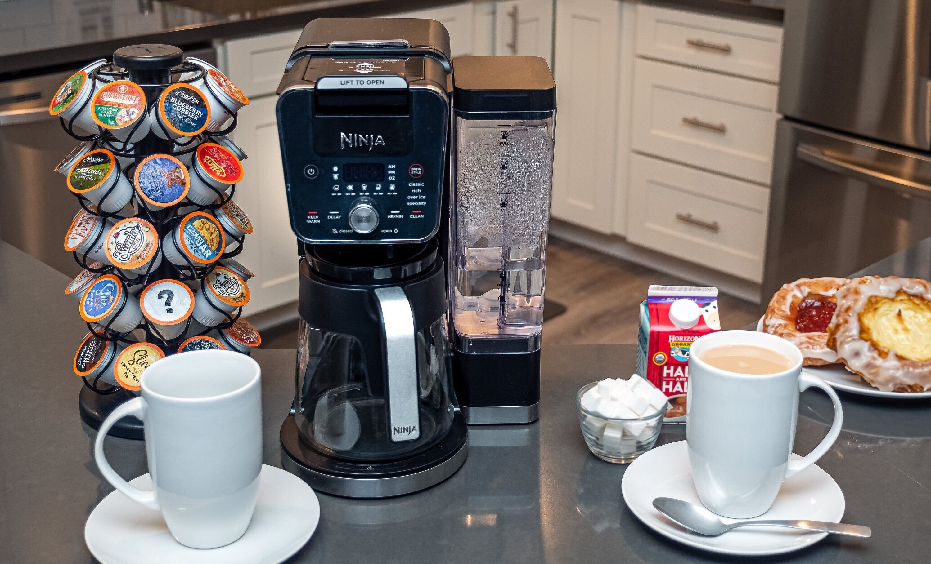 Una macchina per caffè, un portaposate per capsule e due tazze di caffè su un piano di lavoro in cucina.