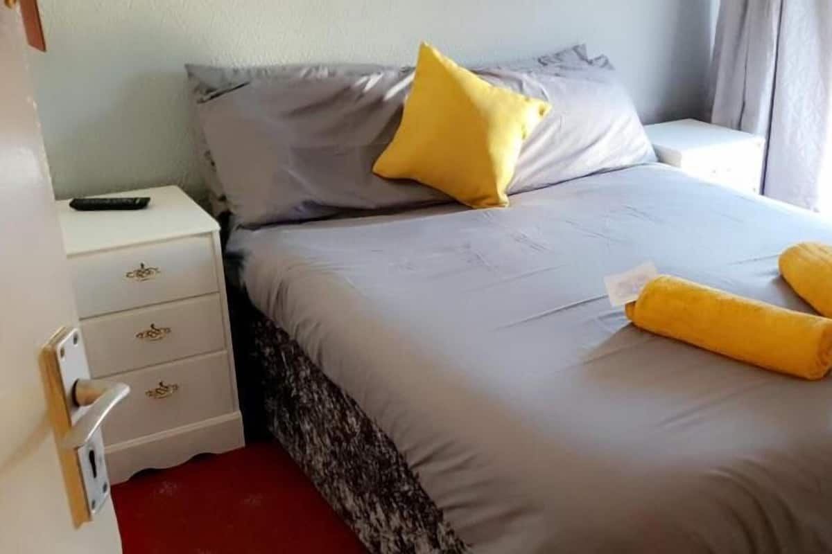 A neatly made bed with pillows and rolled towels, a bedside table with a remote control, and a door with a handle.