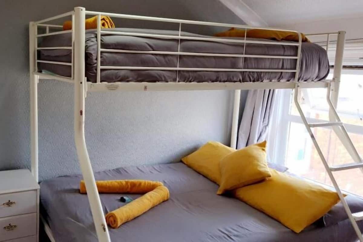 A bunk bed with a grey mattress and yellow pillows, a white dresser with drawers, and a window with curtains.