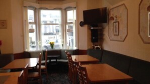 A corner seating area with wooden tables and chairs, a sofa, and a television mounted on the wall. - Bel Reve Hotel (Blackpool)