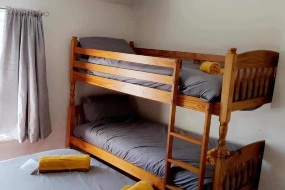 A bunk bed room with a window, curtains, and a bed with a yellow object on it.