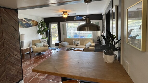 A modern living room with a wooden table, a ceiling fan, and a large window with blinds. - Rock Ridge lll.  Close to everything. (Vero Beach)
